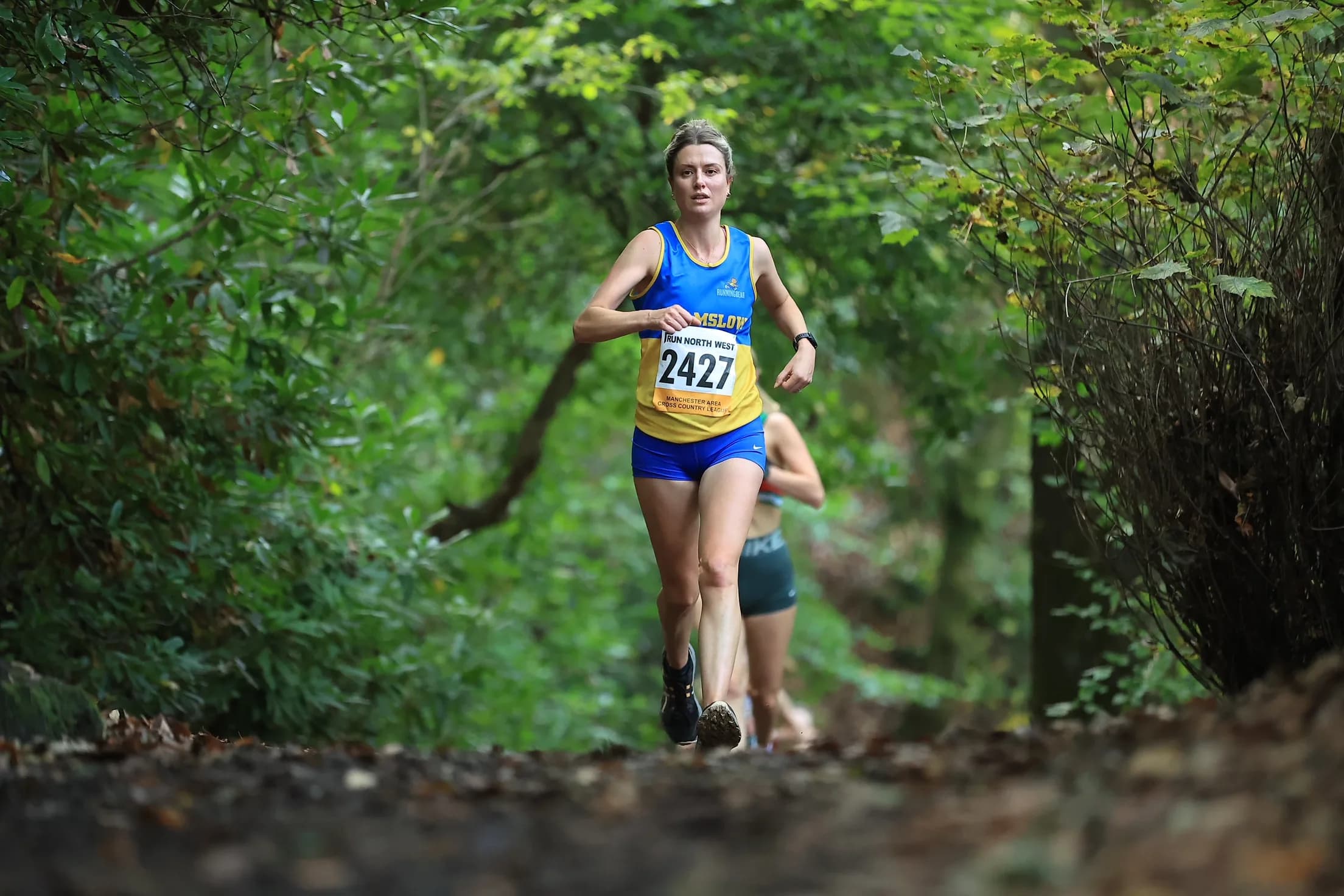 Cross-country runner mid-race on a woodland trail